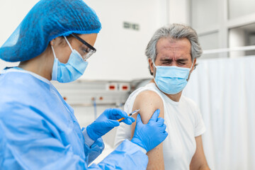 Fototapeta premium Doctor in gloves holding syringe and making injection to senior patient in medical mask. Covid-19 or coronavirus vaccine. Doctor vaccinating male patient in clinic, closeup
