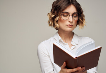 Smart woman with a notebook in her hands and in a white shirt on a gray background cropped view