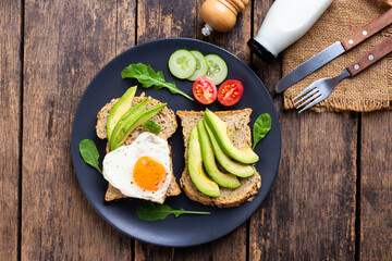 Avocado Sandwich with Fried Egg On black plate on the wooden table