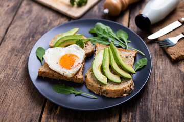 Avocado Sandwich with Fried Egg On black plate on the wooden table
