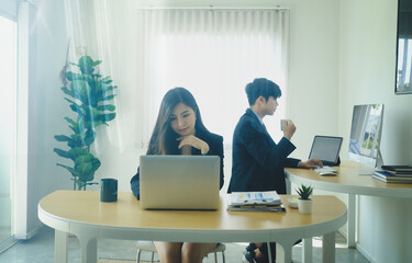 Attractive young woman office worker working with computer laptop and her colleague sitting in background.