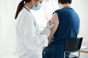 woman doctor in a medical mask injecting a man in a blue t-shirt covid vaccination