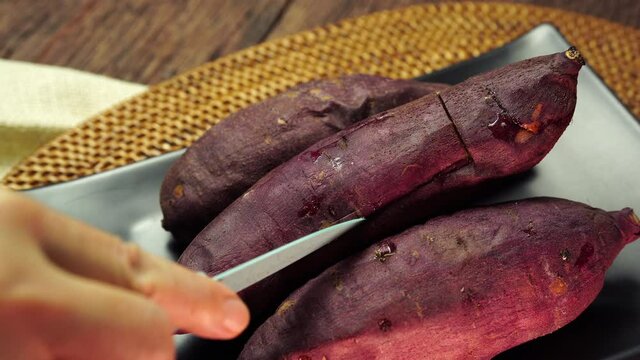 Hand cut and open up baked sweet potato closeup, Japanese Roasted Sweet Potato on wooden table in garden.
