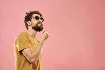 Cute bearded man in a yellow T-shirt dark glasses pink background
