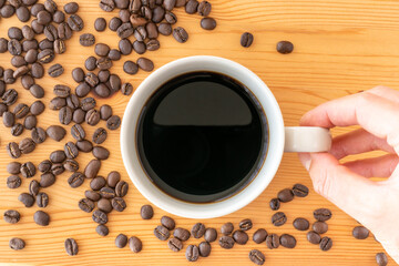 A man’s hand holding a cup of coffee and coffee beans on a wooden table
