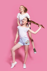Two cheerful excited young women jumping and having fun together over pink background.