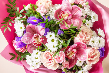 Mother's day, womens day or birthday background. Beautiful bouquet of blooming orchids, carnations and irises and spring greenery on a light pink background.