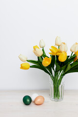 Yellow tulips in a vase and multi-colored eggs on the Easter table