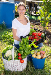 Young woman gardener holding basket with harvest of vegetables in garden outdoor
