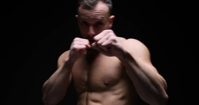 Shirtless muscular sportsman practicing boxing moves in studio