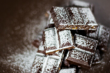 Dark chocolate in powdered sugar. Chunks of dark chocolate.