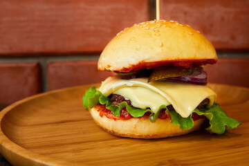 Burger with beef, cheese and lettuce leaves on a wooden plate on a brick wall background. Close-up, selective focus