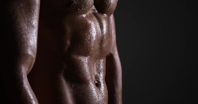 Shirtless muscular man sweating after workout over black background