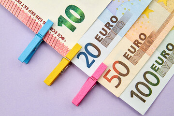 10, 20, 50, 100 Euro banknotes with decorative clothespins on purple background