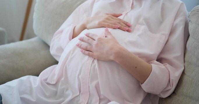 Midsection of pregnant woman caressing her belly while relaxing on sofa