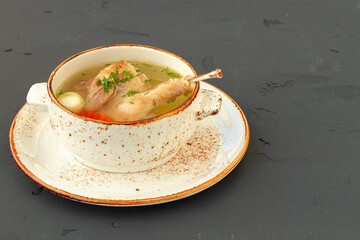 Chicken broth with chicken half in white bowl on gray background