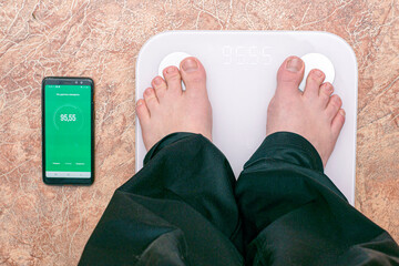 a person is standing on an electronic floor scale next to a smartphone the smartphone has an app...