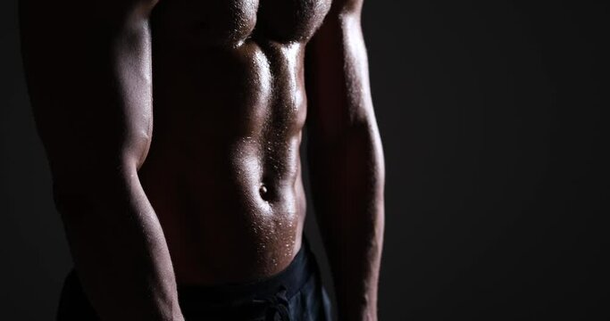 Shirtless muscular man sweating and breathing after workout over black background