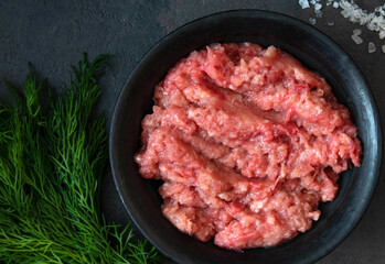 Homemade minced meat in a black bowl with dill. Fresh Raw mince. Top view