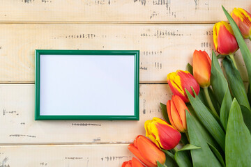 Red tulips on beige background and green photo frame