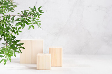 Elegant beige wooden cube podiums with green lush foliage in sunlight on white board and grey marble wall for product display. Simple modern summer design.