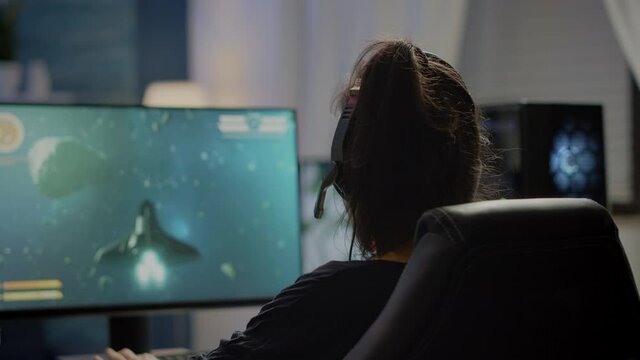 Competitive gamer streatching on gaming chair, putting headphone before playing space shooter video games on RGB powerful computer. Pro woman streaming cyber performing during online esports