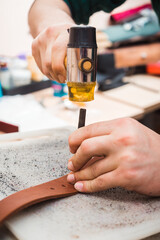 Hammer hits the chisel to make a leather belt.