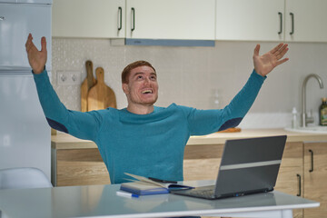 man at home laughing using laptop online, lucky winners. successful young man holding the computer is in a remote location, receiving congratulations, shows his hand yes and cries of delight