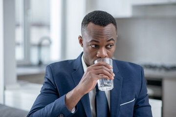 Elegant dark-skinned man looking worried and drinking water