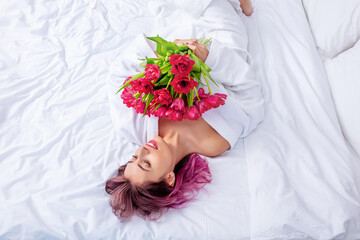 Young adult beautiful happy woman with a bouquet of tulips in the bedroom on the bed in the morning