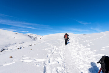 Fototapeta na wymiar Two Hikers on a snowy footpath in winter landscape on the Lessinia Plateau (Altopiano della Lessinia), Regional Natural Park near Malga San Giorgio ski resort, Verona province, Veneto, Italy, Europe.