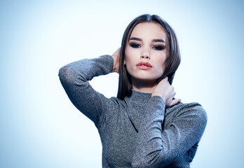 Sexy brunette in a gray sweater on a light background holds her hands behind her head cropped view