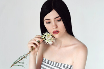 Portrait of beautiful woman's with dark hair and natural makeup with flower in her hands. Skin care or organic cosmetics concept. Cosmetics and makeup.