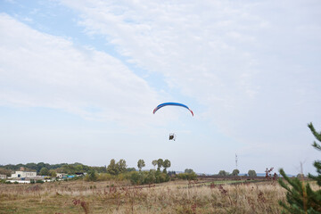 Paratrike with blue parachute flying high in the cloudy sky on autumn morning. Paragliding activity in rural countryside. Weekend leisure time and hobby. Extreme sport flight on paramotor machine.