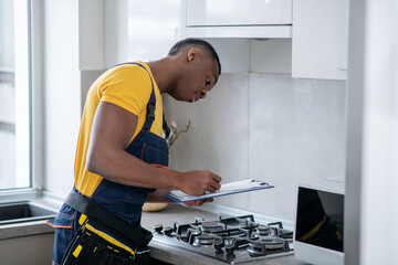 Dark-skinned service man standing near the gas stove in the kitchen