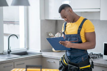 Dark-skinned service man standing in the kitchen and making notes