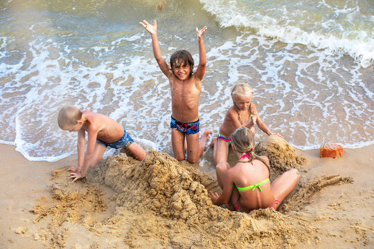 happy tanned children build a sand castle by the sea on the beach on a summer day, horizontal format