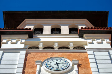 The tower is white with a clock in a tory style. Sunny summer day. Front view.