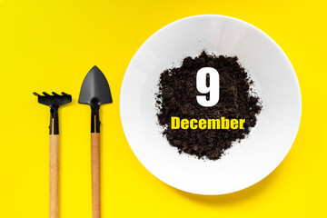 December 9th. Day 9 of month, Calendar date.White plate of soil with a small spatula and rake on...