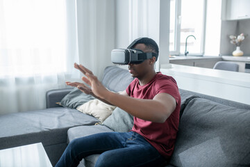 A dark-skinned young man sitting in VR glasses and looking enjoyed
