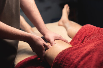 Close-up Masseur man doing thigh massage of the leg to a man athlete client in a dark room of a massage spa