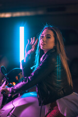Photography with blue and pink neons on a motorcycle from behind. Portrait of a young blonde...