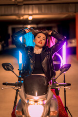 Obraz na płótnie Canvas Photography with blue and pink neons on a motorcycle. Portrait of a young pretty blond Caucasian woman in a black leather jacket