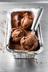 A container of chocolate ice cream and a scoop, several balls, close-up