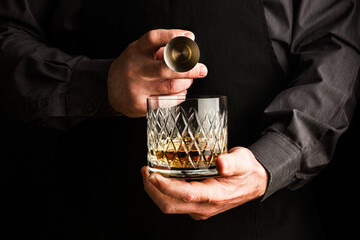 Mano de hombre sosteniendo un vaso de wiskey y un medidor. Vista de frente y de cerca