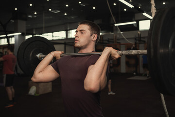 Fototapeta na wymiar Handsome muscular male athlete doing shoulder press with barbell at gym