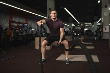 Obraz na płótnie Canvas Strong male athlete exercising with battle ropes at the gym, copy space
