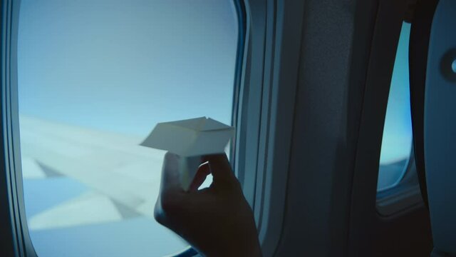 Young adult plays with paper plane inside commercial passenger airplane. Bored during long flight. Excited for travel and flying. New horizons and travel restrictions ban lift
