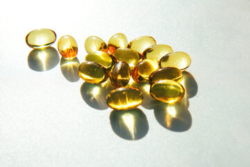 Shiny yellow fish oil capsules on a light background with shadows of focus on the table. Vitamin E