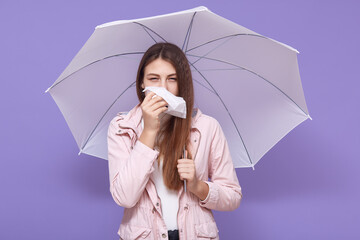Young European sick young female using paper handkerchief, sneezing, having runny nose, standing...